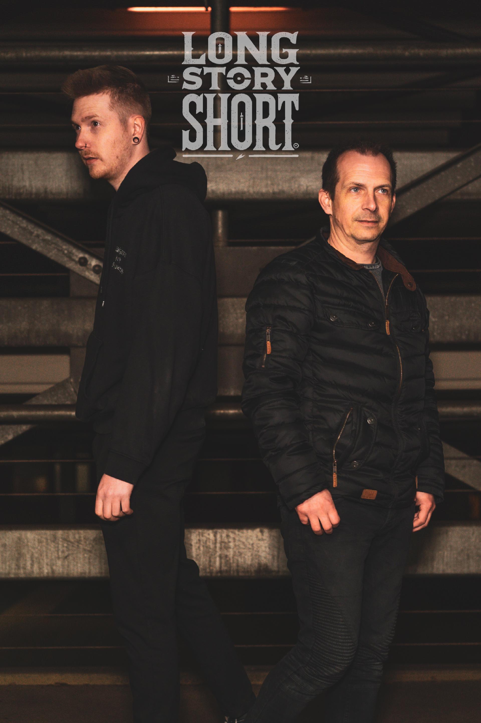 Zwei Männer stehen Rücken an Rücken in dunkler Kleidung vor Metallstruktur, Schrift: "Long Story Short"