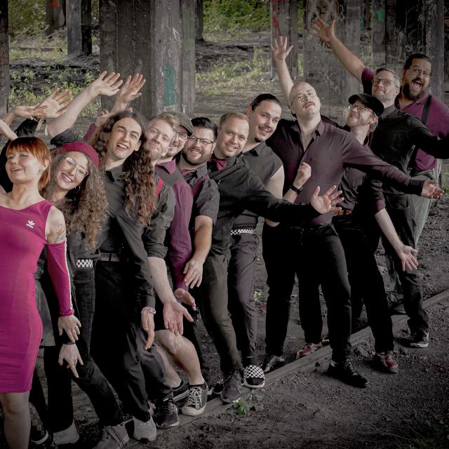 Die Band auf einem Industriegelände in ihrem Outfit, geprägt von der Farbe Schwarz und Bordeaux.