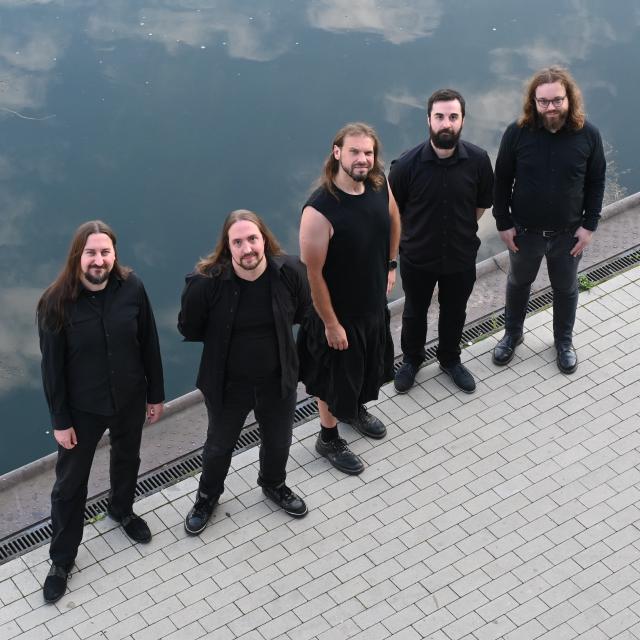 Die Band Oceansoul steht auf einer Kaimauer an einem ruhigen, trüben Gewässer.